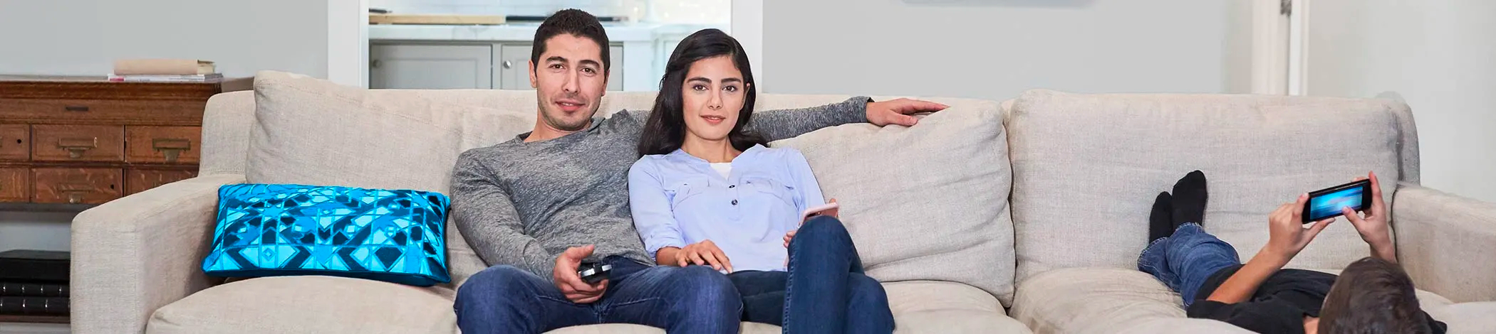 Par bruger tv-fjernbetjening i sofaen, mens barnet bruger smartphone