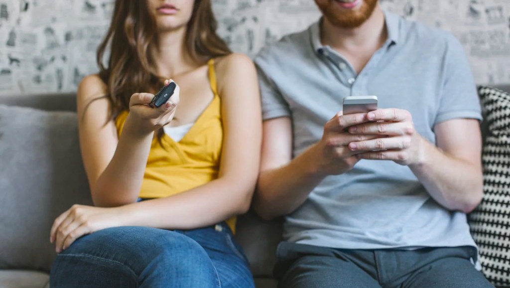 Woman using TV remote, man using smart phone